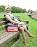 Clothed female with blonde hair shows off her red pumps in nylons on a bench